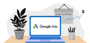 A flat-design vector illustration of a workspace desk, updated with a minimalist color palette featuring near black, white, electric blue, and cool gray. On a light wooden desk sits a laptop with an electric blue chassis and keyboard. The laptop screen is bright white and displays the Google Ads logo in its original colors alongside the text "Google Ads" in near black. To the left of the laptop is a potted plant with solid near-black leaves in a cool gray pot. To the right is a cool gray pencil cup holding several near-black pencils. In the background, a cool gray calendar hanging on a white wall shows a timeline numbered 11, 12, 1 through 7, with an electric blue line graph trending upward toward a bold, black dollar sign ($). | How Much Do Google Ads Cost in Australia? (2026 Guide)